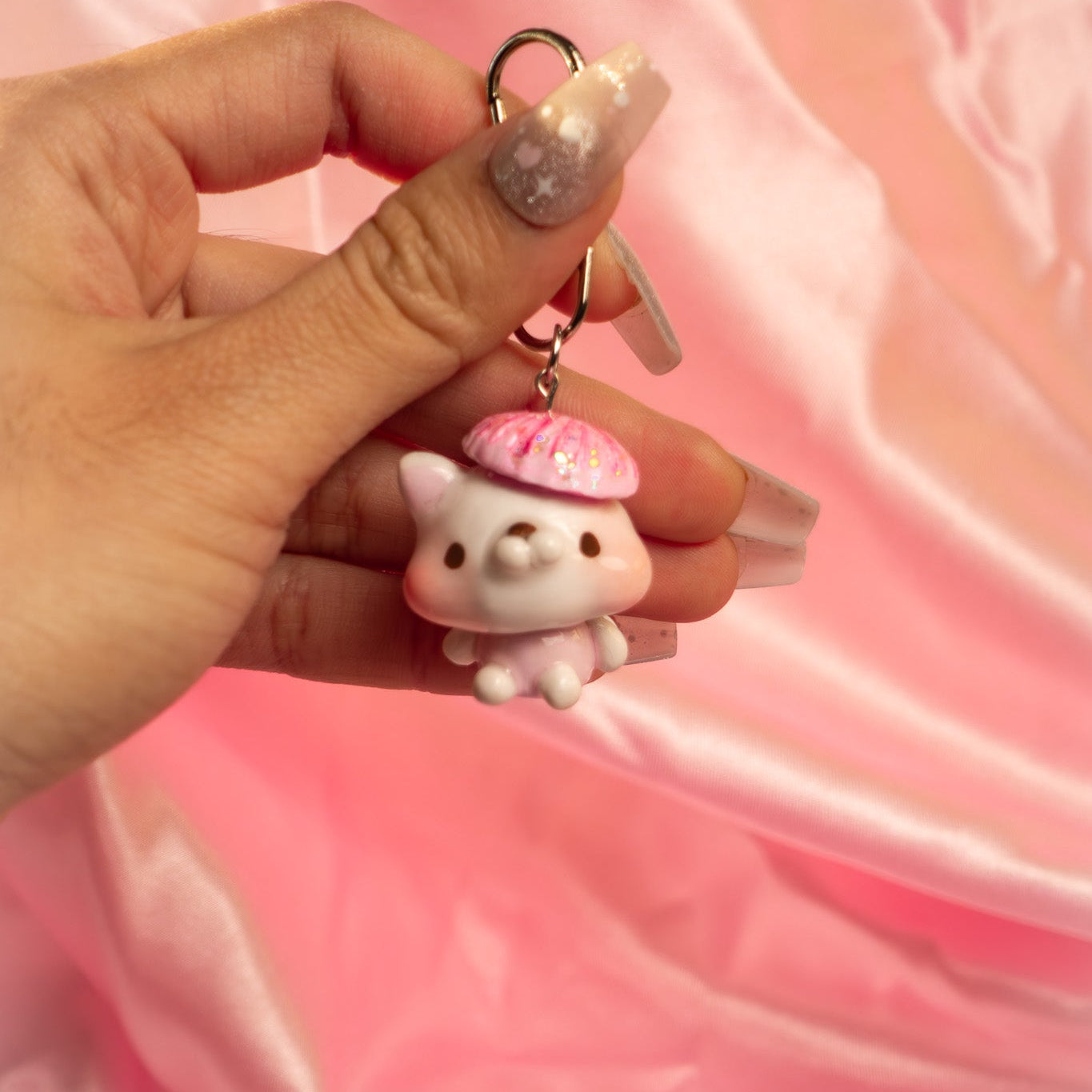 Hand holding a small pink and white cat-shaped keychain against a pink background